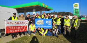 Group of volunteers stands near gas station, smiling while holding up signs with the nonprofit's name.