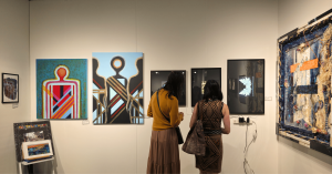 Visitors standing near a gallery wall, observing and discussing contemporary paintings and mixed media artworks at a TERAVARNA exhibition.
