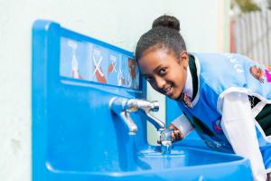 Schoolgirl drinking clean water from a fountain in Africa