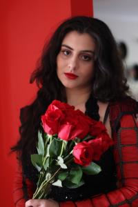 Tamara Mechael holding red roses in a red and black outfit, photographed by Tyler Disney for a music press release highlighting her songwriting success.