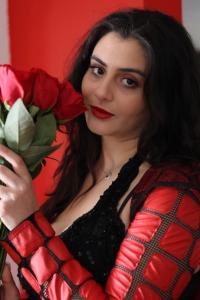 Close-up of Tamara Mechael holding roses near her face, wearing a black and red outfit, photographed by Tyler Disney.
