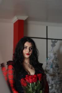 Tamara Mechael in a red and black outfit holding a bouquet of red roses during a studio photoshoot by Tyler Disney.