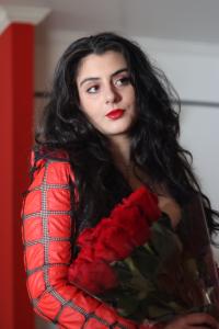 Tamara Mechael facing forward holding red roses, wearing a black and red outtit, photographed by Tyler Disney for press use.