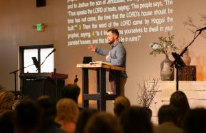 Pastor Joe DuCharme preaching from the pulpit with Bible open and scripture projected on screen at Calvary Chapel The Rock in Santa Rosa California