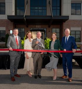 Five leaders from Gray Operations Group, Thompson Gray, and Gray Analytics stand in front of their Huntsville office, smiling as they cut a red ribbon during the grand opening ceremony.