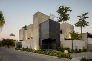 Contemporary architecture studio in Colima featuring exposed concrete volumes, a black steel facade entrance, landscaped edges, and tropical trees integrated into the design.