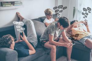 Four children sit together on a couch, each looking at their own phone, with illustrated chat bubbles floating above them.