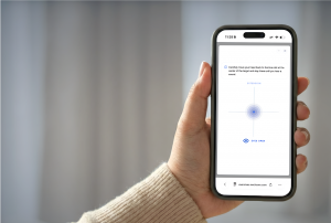 Hand holding a smartphone showing the NeckCare home exercise screen with a central target, “eyes open” guidance, and instructions to move the head to the blue dot.