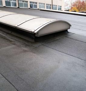 Close-up of a waterproofed black bitumen flat roof surface with a large curved skylight on a commercial building.