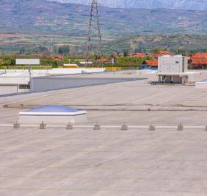 Wide-angle view of a professionally installed industrial flat roof system with a skylight and HVAC unit, overlooking a residential area with mountains in the background.