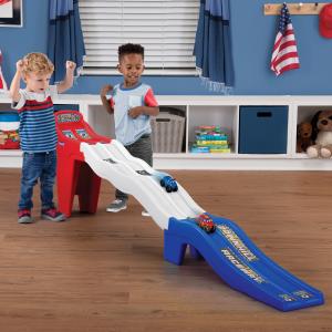 Two boys playing with a red, white, and blue racetrack. Two cars are sliding down.