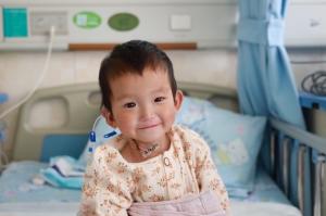 Young child recovering in hospital bed smiling after heart surgery through LWB's cardiac program