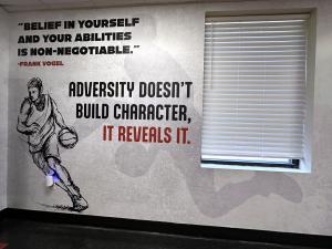 Wall graphic at the JD Lewis Center with an illustrated basketball player and Frank Vogel quotes about belief, adversity, and character beside a window.