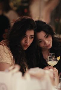 Two girls with cocktails taking selfies at a private dinner table during an event.