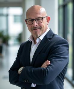 Professional headshot of Jimmie Applegate in navy blazer with arms crossed in modern office setting
