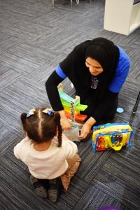 a therapist and child are sitting together on the floor while playing with cars.