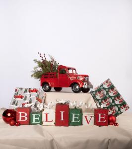 Interior Christmas décor display with a red truck, wrapped gifts, ornaments, and BELIEVE blocks styled on a tabletop.