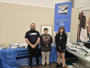 a man stands in front of a blue tablecloth with 2 scholarship winners