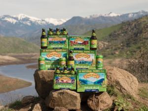 Green Sierra Nevada cans, bottles and packaging of Pale Ale sit on brown rocks with a winding river and snowy mountains in the background.