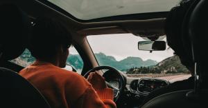 Two people in the front seats of a car driving through mountains, captured from the back seat with a scenic road ahead, enabled by Luup car sharing Vancouver