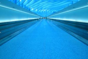 A blue tunnel with moving walkway in blue terrazzo with blue lighting and wavy art installation on the ceiling