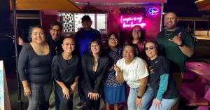 A group of people pose together outdoors at night in front of a food truck with neon lighting. Lumpia by Bebot owner Mykyl Hatch stands at the center, surrounded by members of the Philippine American Chamber of Commerce–Greater San Antonio during Lumpia W