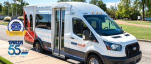 A white and red paratransit van parked on a street near a sidewalk, with logos celebrating TARTA's 55 years and Certified Autism Center status.