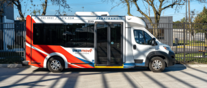 Small white and red Paratransit shuttle bus parked on a street with trees and buildings in the background.
