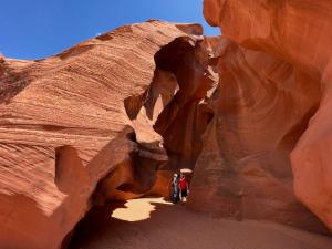 Visitors walking through a narrow red sandstone slot canyon with smooth curved walls and sunlight illuminating the passage.
