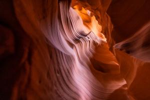 Abstract curves of smooth sandstone inside a slot canyon with warm light illuminating the layered rock formations.