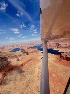 Aerial view from a small aircraft showing Lake Powell surrounded by red rock desert terrain and winding waterways.
