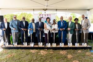 A group of community leaders, elected officials, and development partners stand side by side under a tent, each holding a ceremonial shovel in front of a Pearl Ridge sign, during the groundbreaking event for the new residential community in Southern Dalla