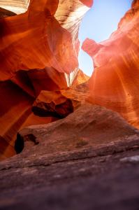 Upward view inside Antelope Canyon showing smooth red sandstone walls and natural light shining through a narrow opening above.