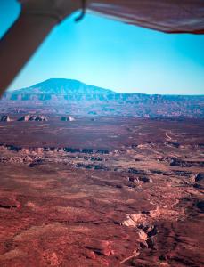 Aerial view of a vast desert landscape with layered rock formations, mesas, and distant mountains under a clear sky.