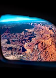 View of a vast canyon landscape seen through the window of a small aircraft, showing red rock formations and winding terrain below.