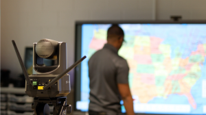 A Clear Touch Command Studio wireless PTZ camera mounted on a tripod, featuring dual antennas and 20x optical zoom for professional mobile broadcasting in a classroom or office setting.