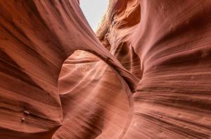 Smooth red sandstone walls forming a natural arch inside a narrow slot canyon with soft light filtering from above.