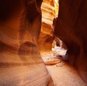 A tight slot canyon pathway with curved red rock walls and sandy ground leading deeper into the canyon.