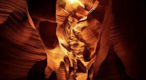 Interior of a slot canyon glowing with warm golden light, showing layered sandstone textures and narrow passageways.