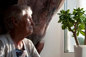 Older woman sitting by a window at home, looking outside in quiet reflection