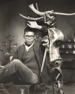 A young Richard Hunt posing with his arm above his head, resting on a metal abstract sculpture.