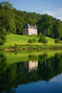 A building that looks like a historic castle on a spring green hill surrounded by trees with a river in the foreground