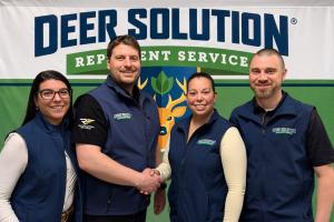 Mariana and Matt Norman (right) shake hands with co-founders Kris and Jaime Goodrich (left) in front of a backdrop of the Deer Solution logo.