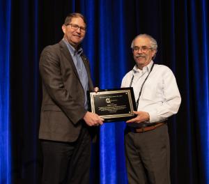 Mike Croke accepting Peter M. Mayo award at the CI Annual Meeting in Houston, TX. Mike has a proud smile and is holding his plaque.