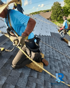 Professional Rainforcing Roofing experts wearing safety harnesses while installing new shingles on a steep residential roof.
