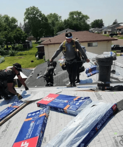 Rainforcing Roofing experts in safety harnesses installing GAF Timberline HDZ shingles on a residential roof. Bundles of premium shingles and high-quality underlayment are visible as the team works on a full system replacement.