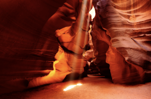 A shaft of sunlight reaches the floor of Antelope Canyon, highlighting layered sandstone formations.