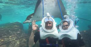 John the Dolphin Expert and his wife wearing SeaVenture dive helmets underwater at Discovery Cove Orlando while a large ray swims above them.