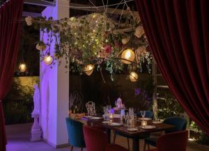 A candlelit dining table set beneath a floral chandelier of roses and trailing greenery, framed by deep red velvet curtains, at Five Seasons in Ragusa, Sicily — the intimate setting for The Requiem, a 12-course narrative gastronomy experience created by G