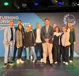 The Sustainability Awards team standing on stage, smiling in front of a branded event backdrop.
